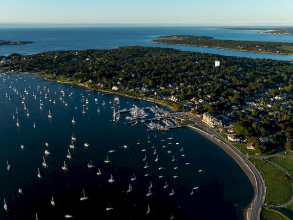 Aerial view of a coastal town with numerous boats anchored in the water, lush greenery, and a winding road along the shoreline.