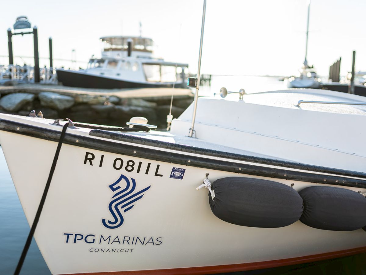 A close-up of a boat at a marina, showing the hull with a &ldquo;TPG MARINAS&rdquo; logo and registration RI 0811, docked near calm water.