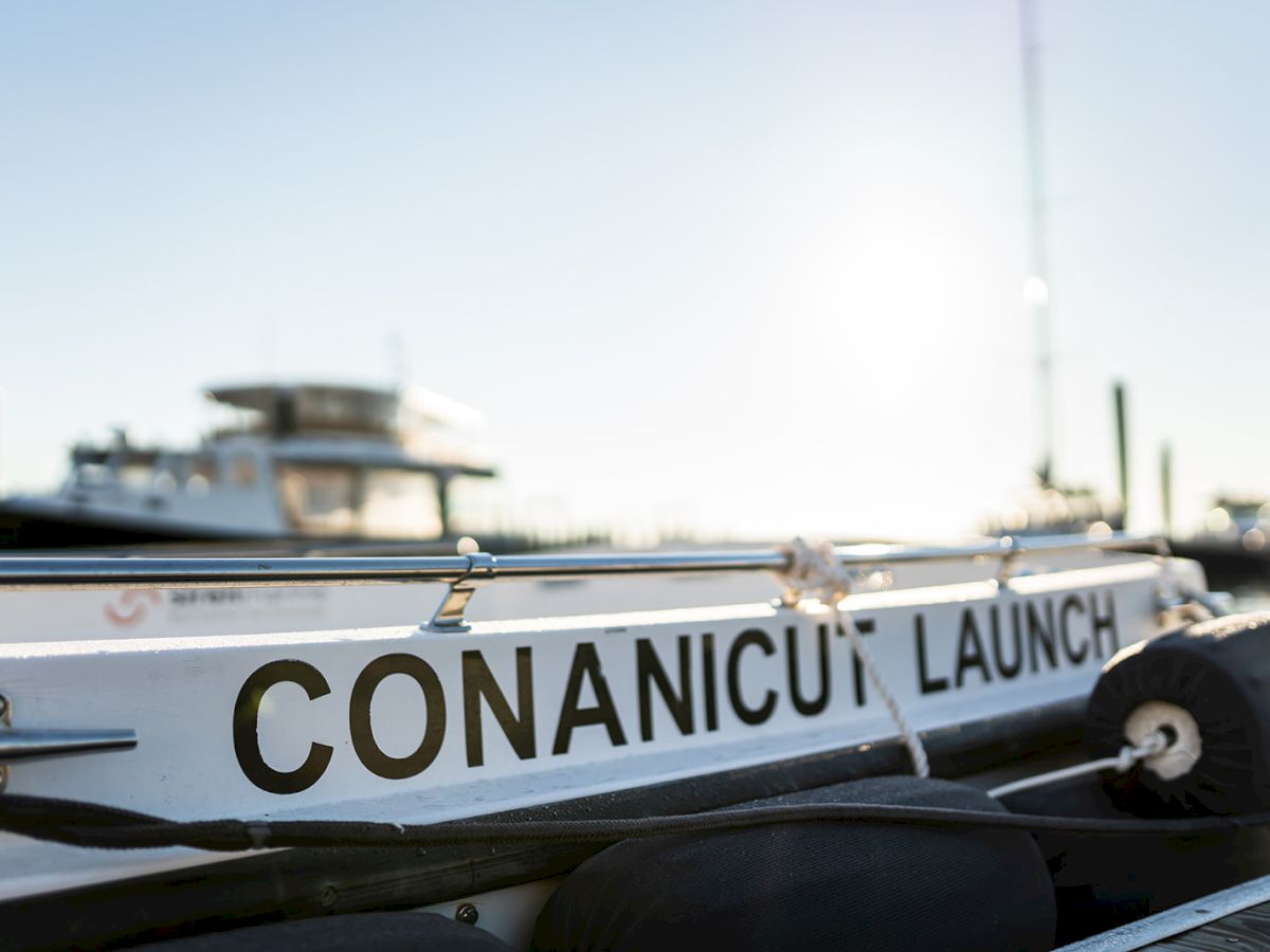 A boat named "CONANICU LAUNCH" is docked at a pier, with sunlight and other boating equipment in the background.