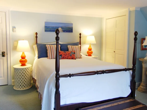 A luxurious bedroom with a dark wooden four-poster bed, white bedding, striped pillows, two matching nightstands, lamps, and a soft blue-clad decor, soothing light.