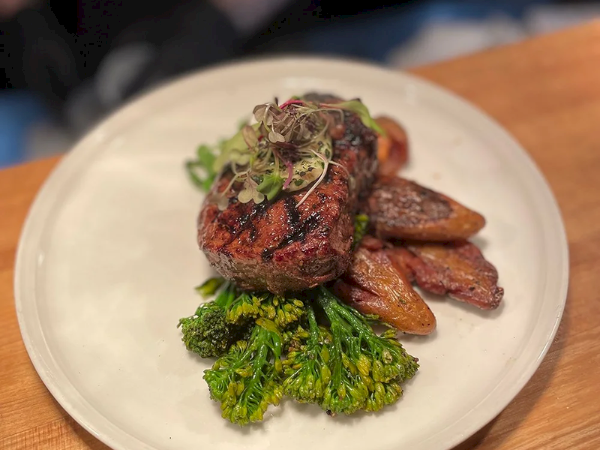 Seared steak medallions with crispy roasted potatoes and broccoli, topped with microgreens on a white plate.