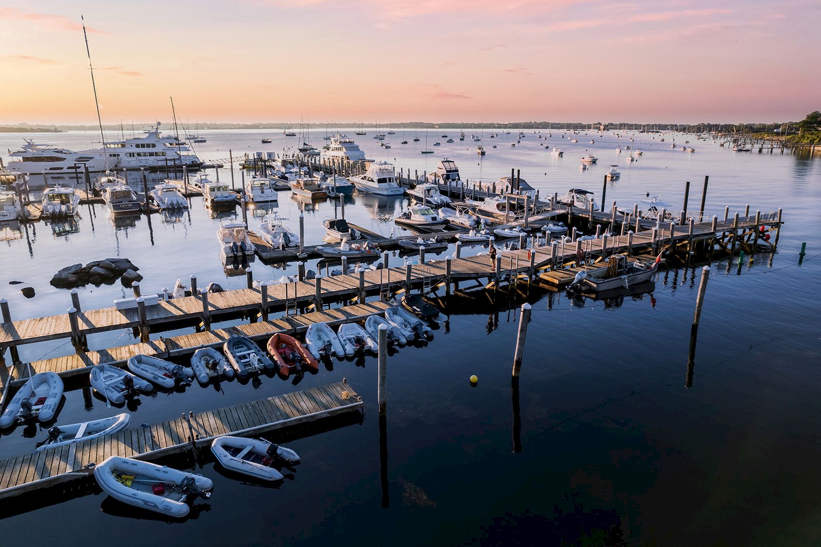 Boats and a long wooden pier at a calm marina at sunset, with calm water reflecting pink skies and several small boats docked along the pier.