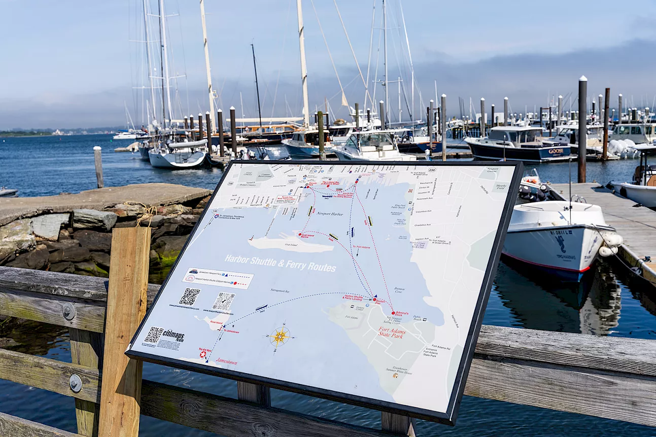 A harbor scene with boats docked at piers and a large map sign on a wooden railing, guiding visitors around the marina.