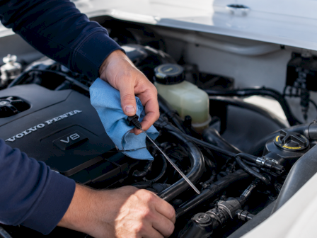 A person hoses down a car engine, wiping a component with a blue cloth under a hood.