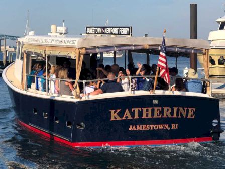 A blue tour boat named &ldquo;KATHERINE&rdquo; with passengers seated, docking at a marina in Jamestown, RI, American flag visible.