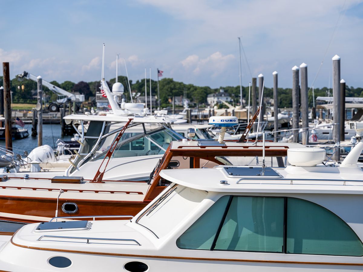 A marina filled with docked motorboats and yachts, with calm water and clear sky in the background.