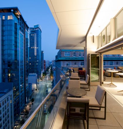 A high-rise city view with modern buildings and a balcony featuring tables and chairs, taken during dusk.