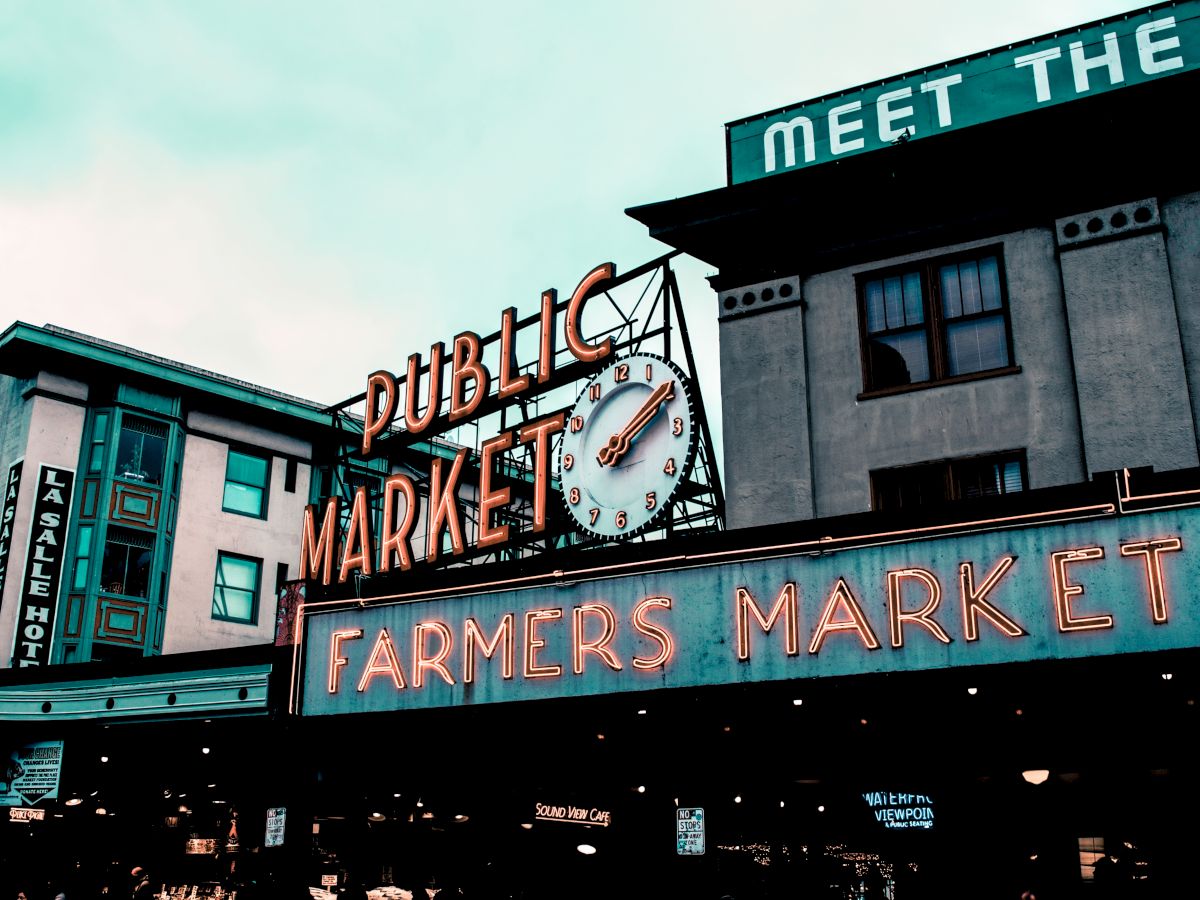 The image shows the exterior of a public market building with a large sign that reads "Public Market" and "Farmers Market." It includes a clock.