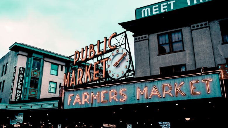 The image shows the exterior of a public market building with a large sign that reads "Public Market" and "Farmers Market." It includes a clock.